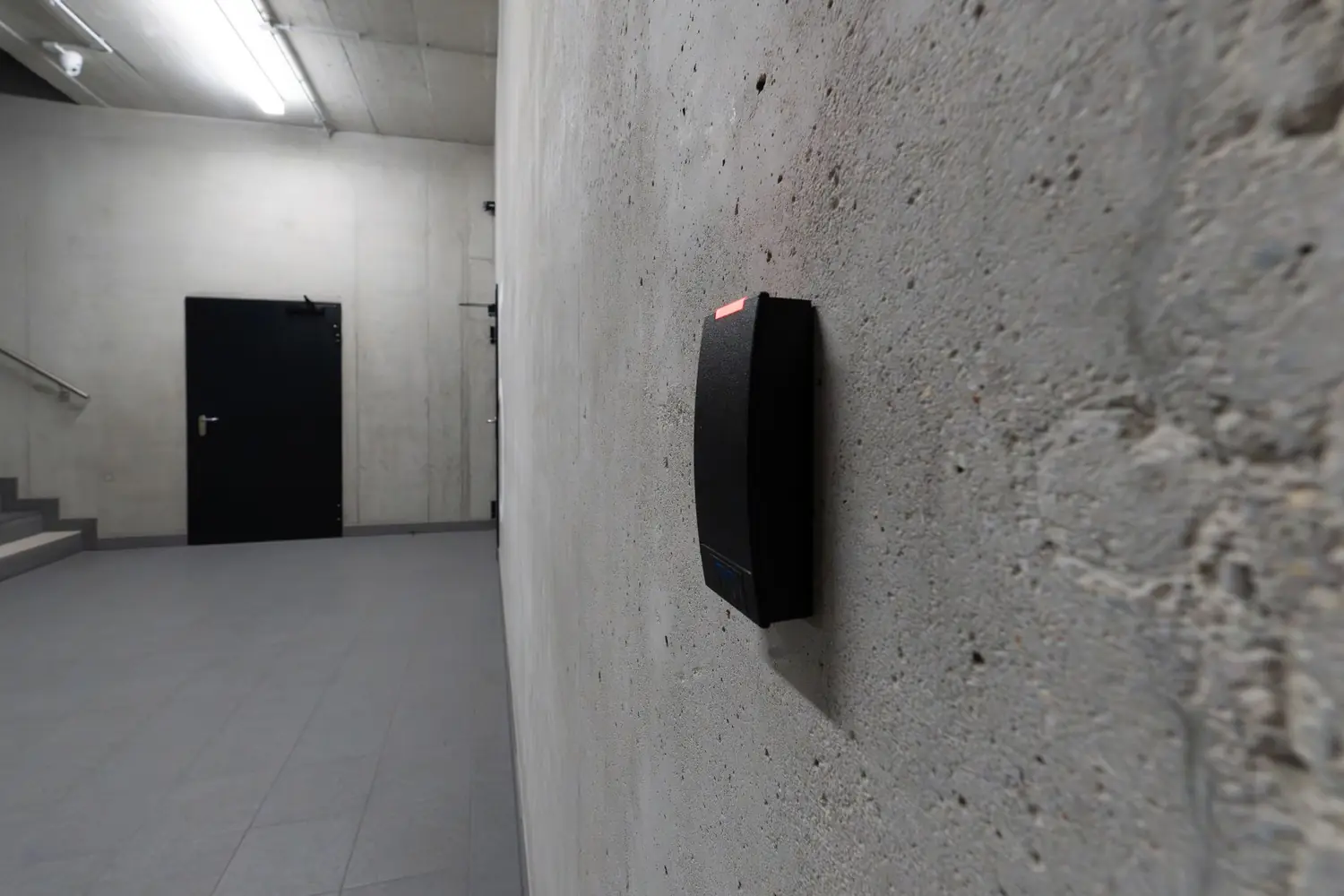 Electronic access-control card reader on a concrete wall beside a corridor