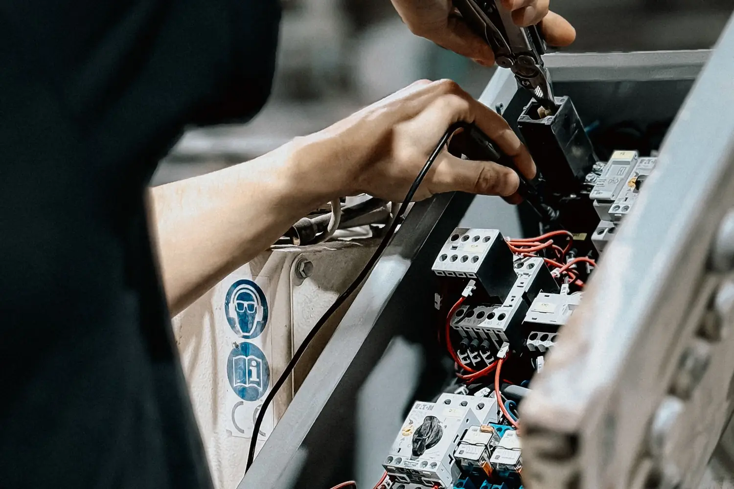 Technician using hand tools on wiring inside an open industrial control cabinet